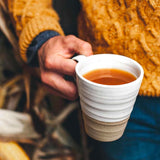 Person holding a white ceramic mug with a beige base, wearing a mustard yellow sweater.