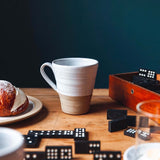 Ceramic mug on a wooden table with dominoes and a pastry.