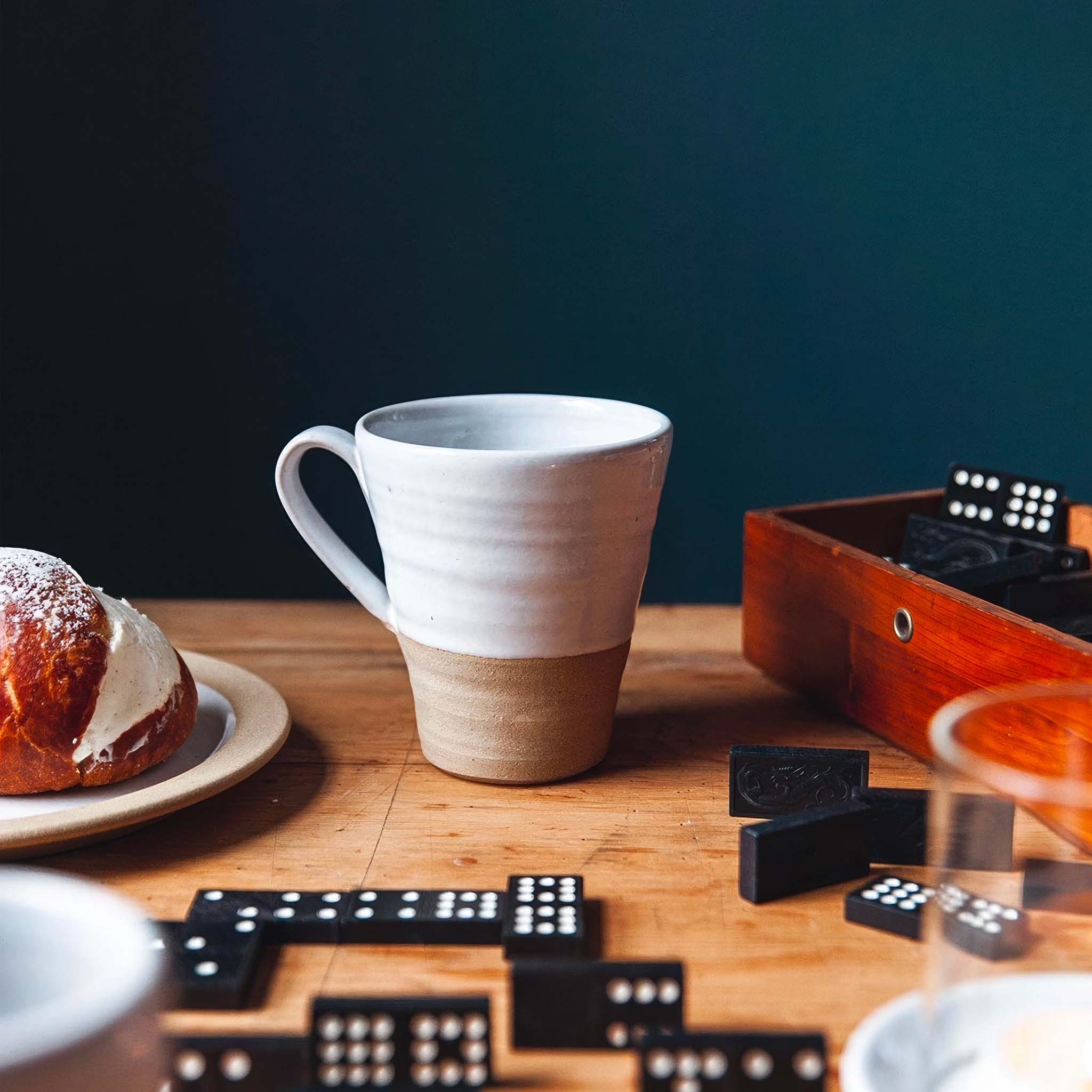 Ceramic mug on a wooden table with dominoes and a pastry.