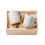 Two white ceramic mugs in a wooden gift box with straw padding on a white background
