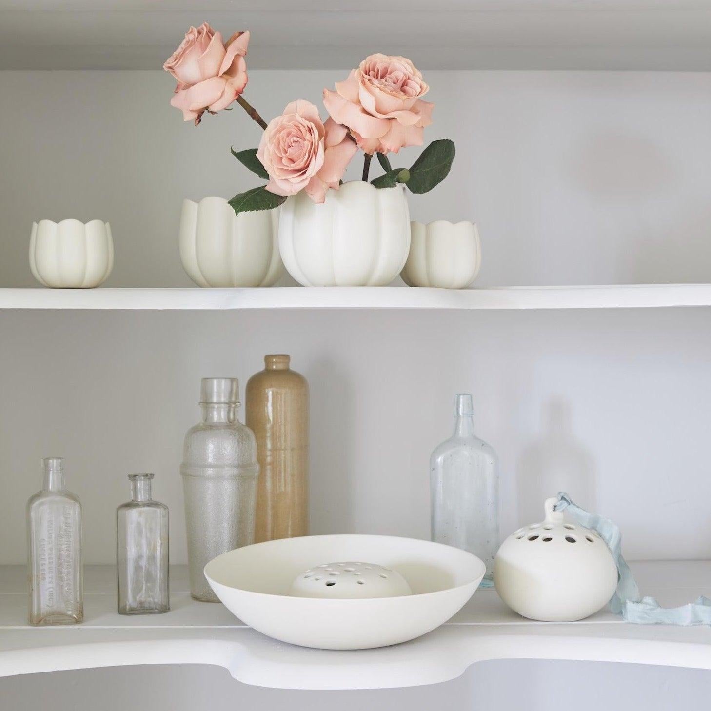 Shelf display featuring small and large white ceramic frog vases, styled with blush roses and surrounded by neutral-toned glass bottles and vessels.