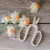 Grey clippers with floral handles on a wooden surface with white flowers.