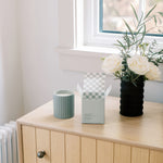 A lifestyle image of Hudson + Oak's Sage candle and its box sits open on a wood wardrobe chest.