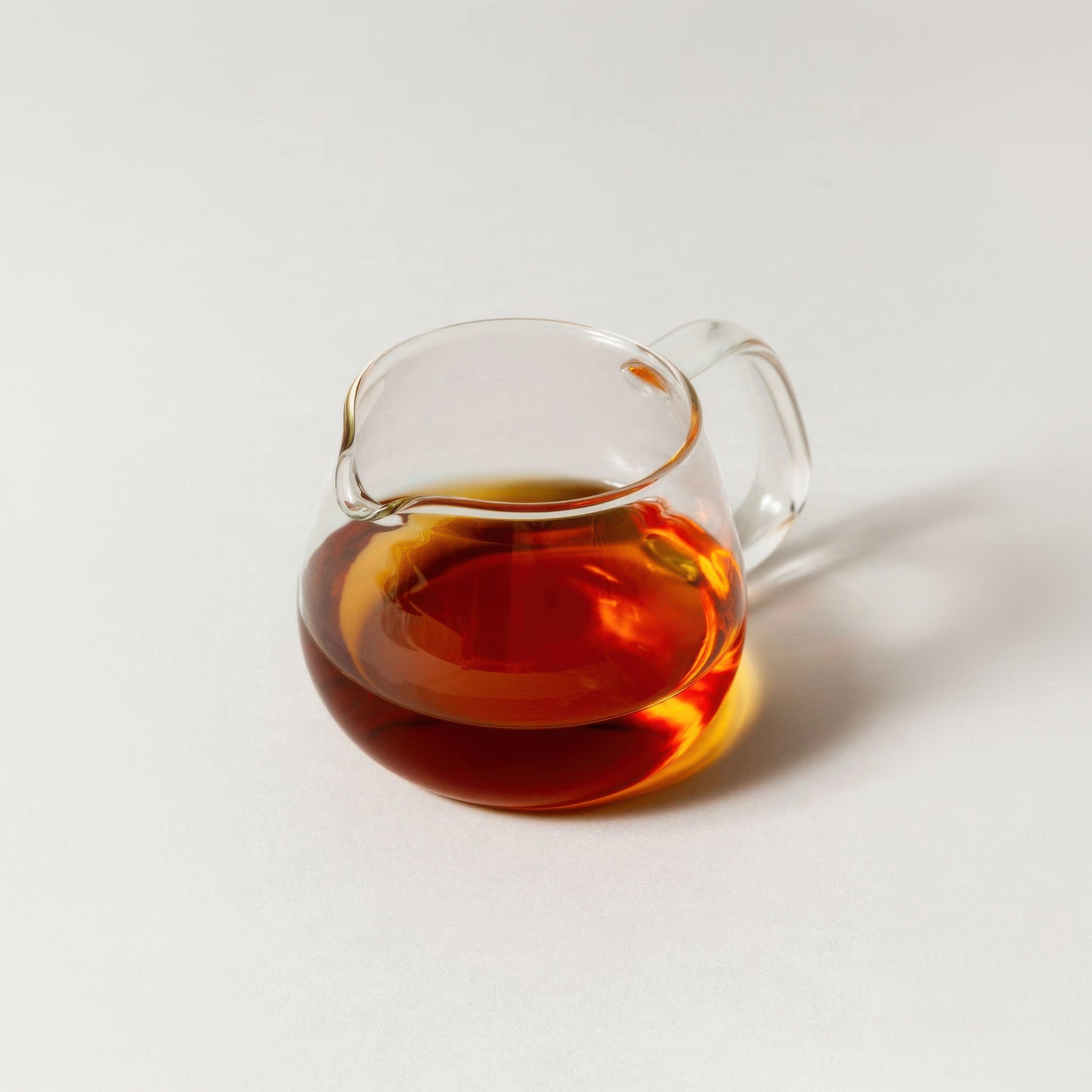 Clear glass cup of hojicha on a light gray background