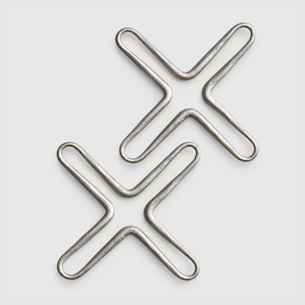 Two metallic silver X-shaped wire or metal trivets on a light gray background.