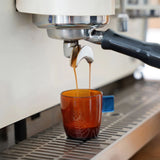 Espresso being poured from a machine into an amber glass cup.
