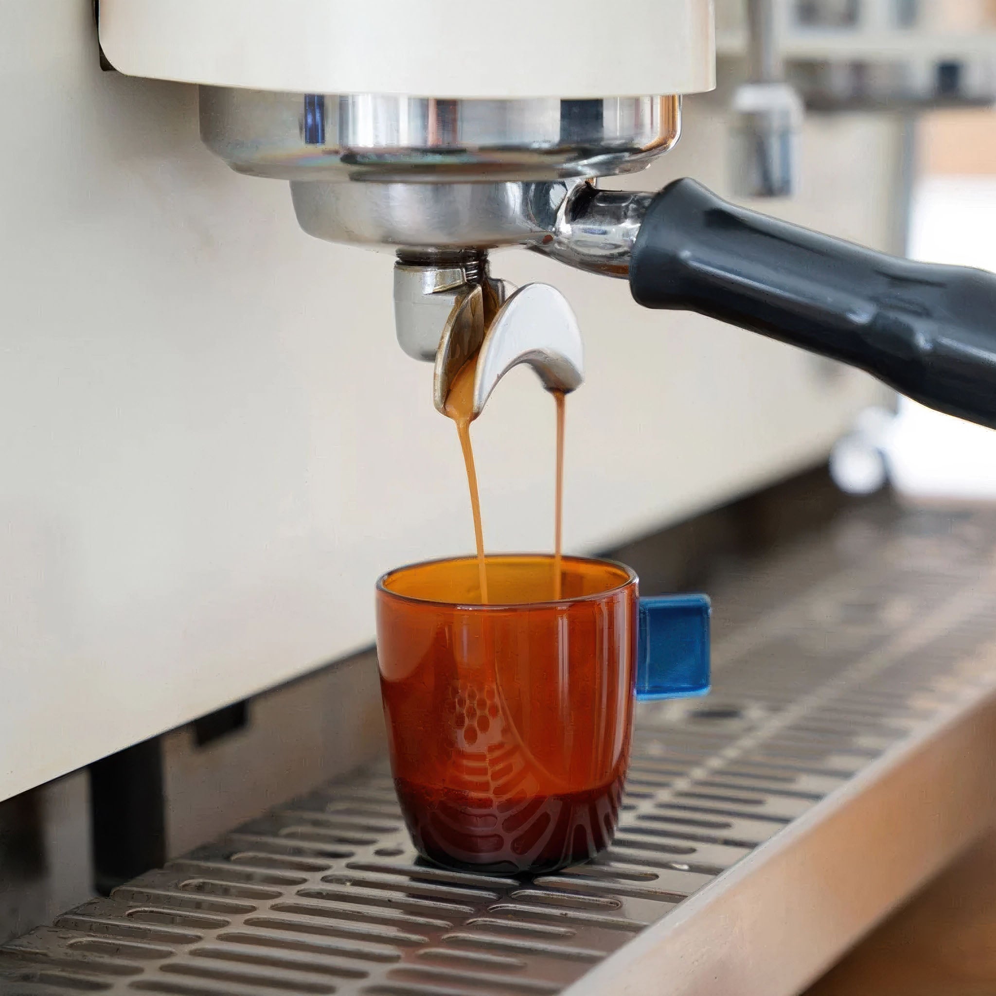 Espresso being poured from a machine into an amber glass cup.