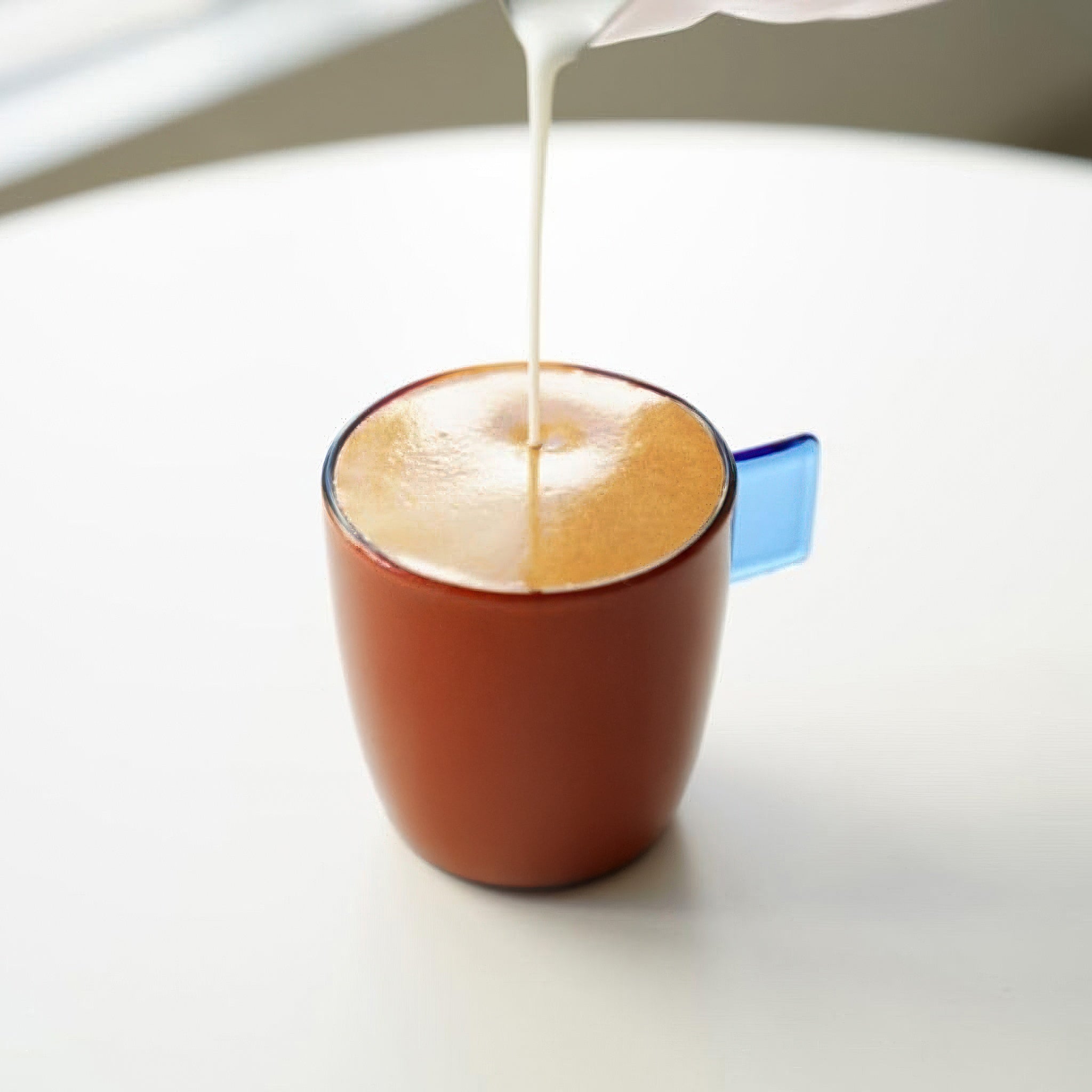 Steamed milk being poured into a coffee cup on a white background