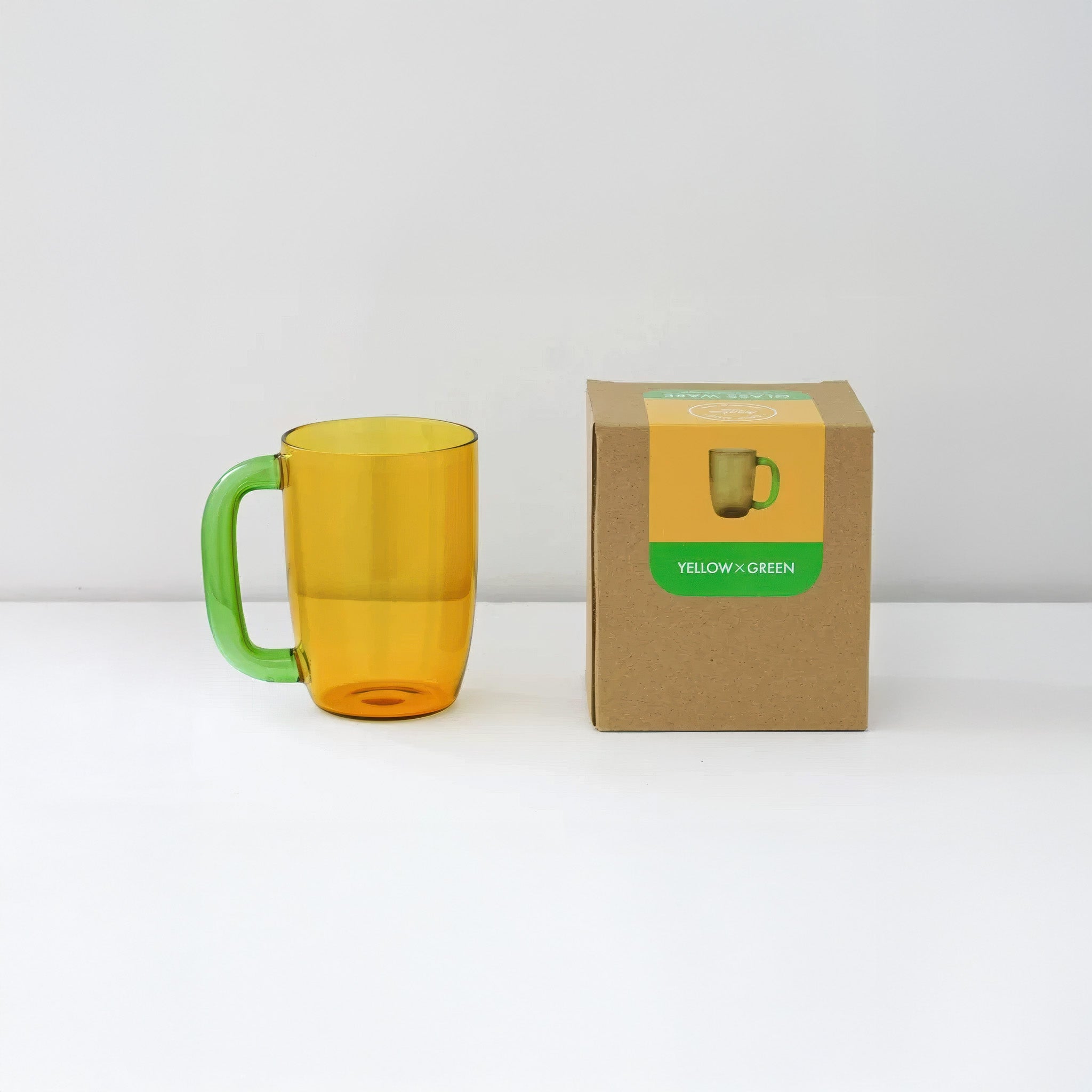 Yellow mug with green handle next to its packaging on a white background