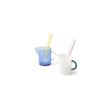 Two glass mini pitchers with colorful spoons on a white background