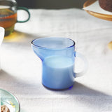 Blue glass mini pitcher with white handle on a light fabric surface