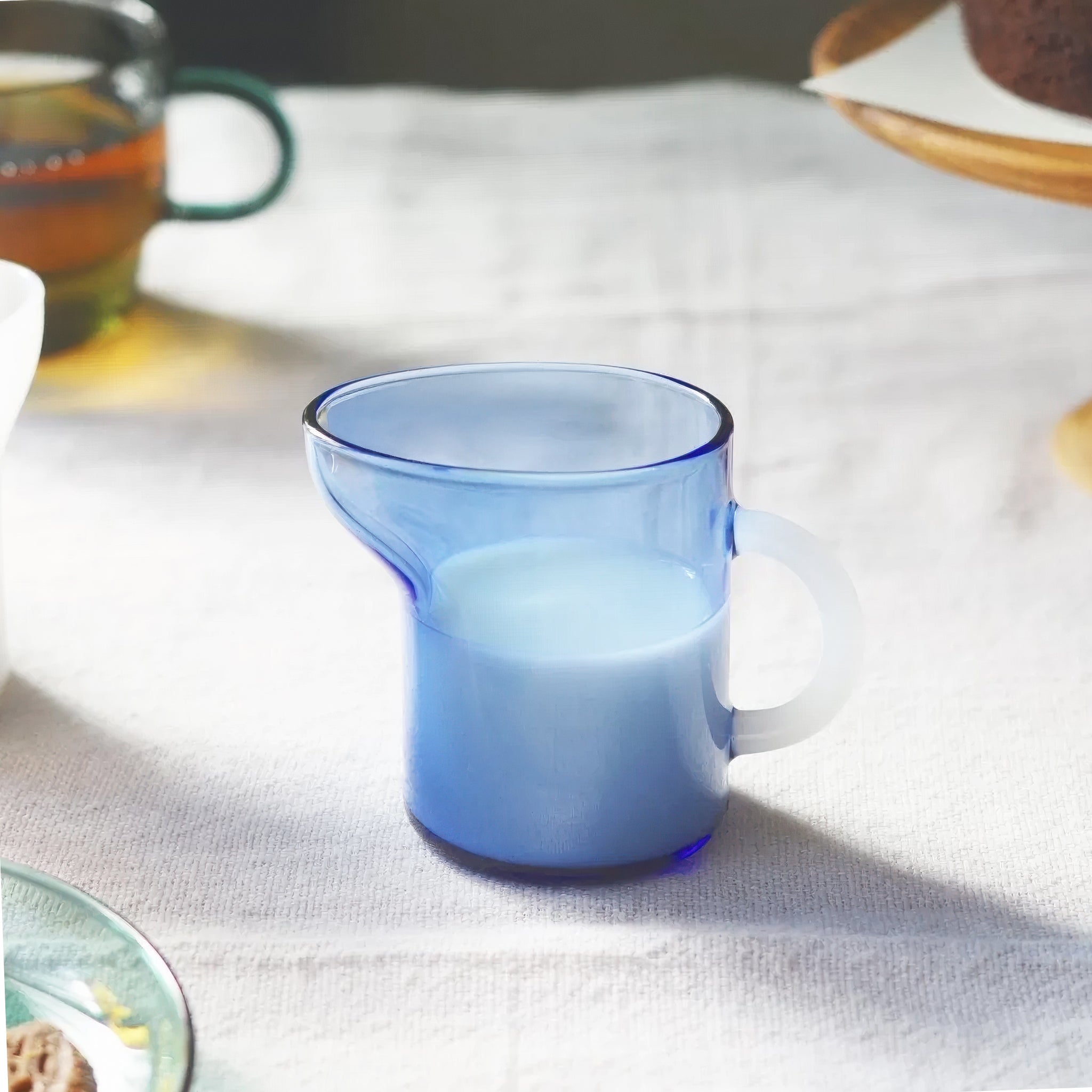 Blue glass mini pitcher with white handle on a light fabric surface