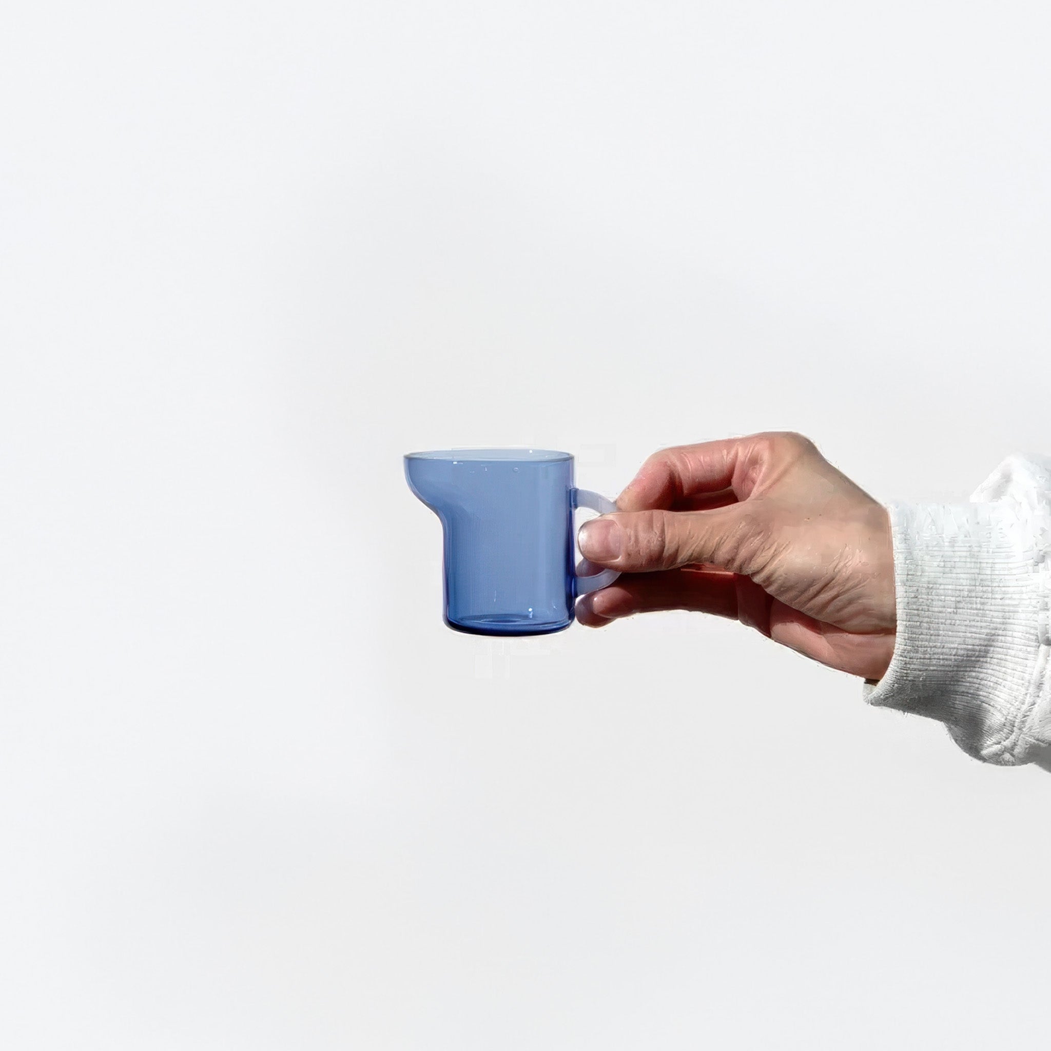 Hand holding a mini blue pitcher against a white background