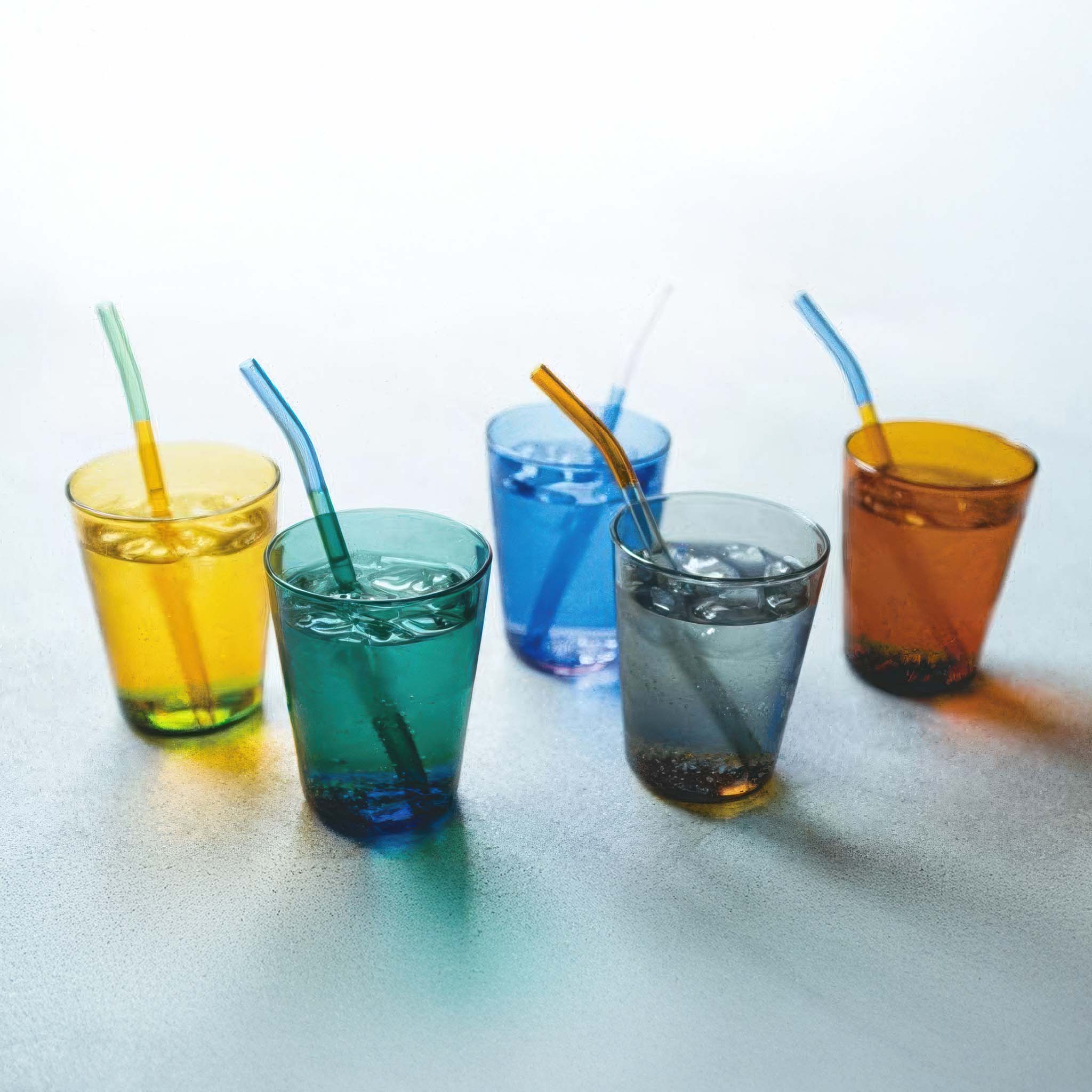 Five colored glasses with straws on a light surface