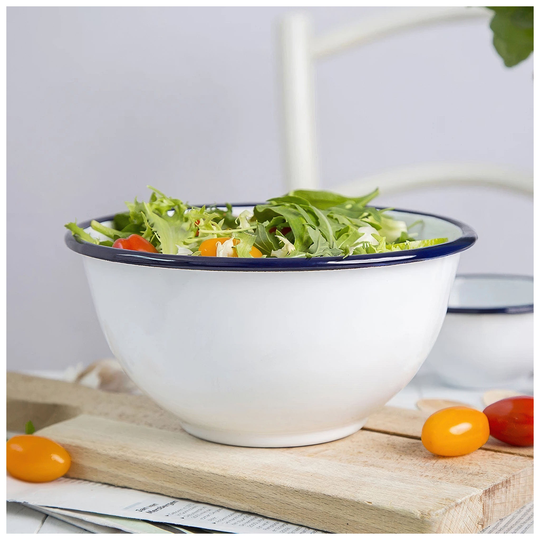White enamel bowl with a navy rim holding a fresh green salad on a wooden board.