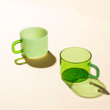 Two green mugs, one ceramic the other glass on a beige background