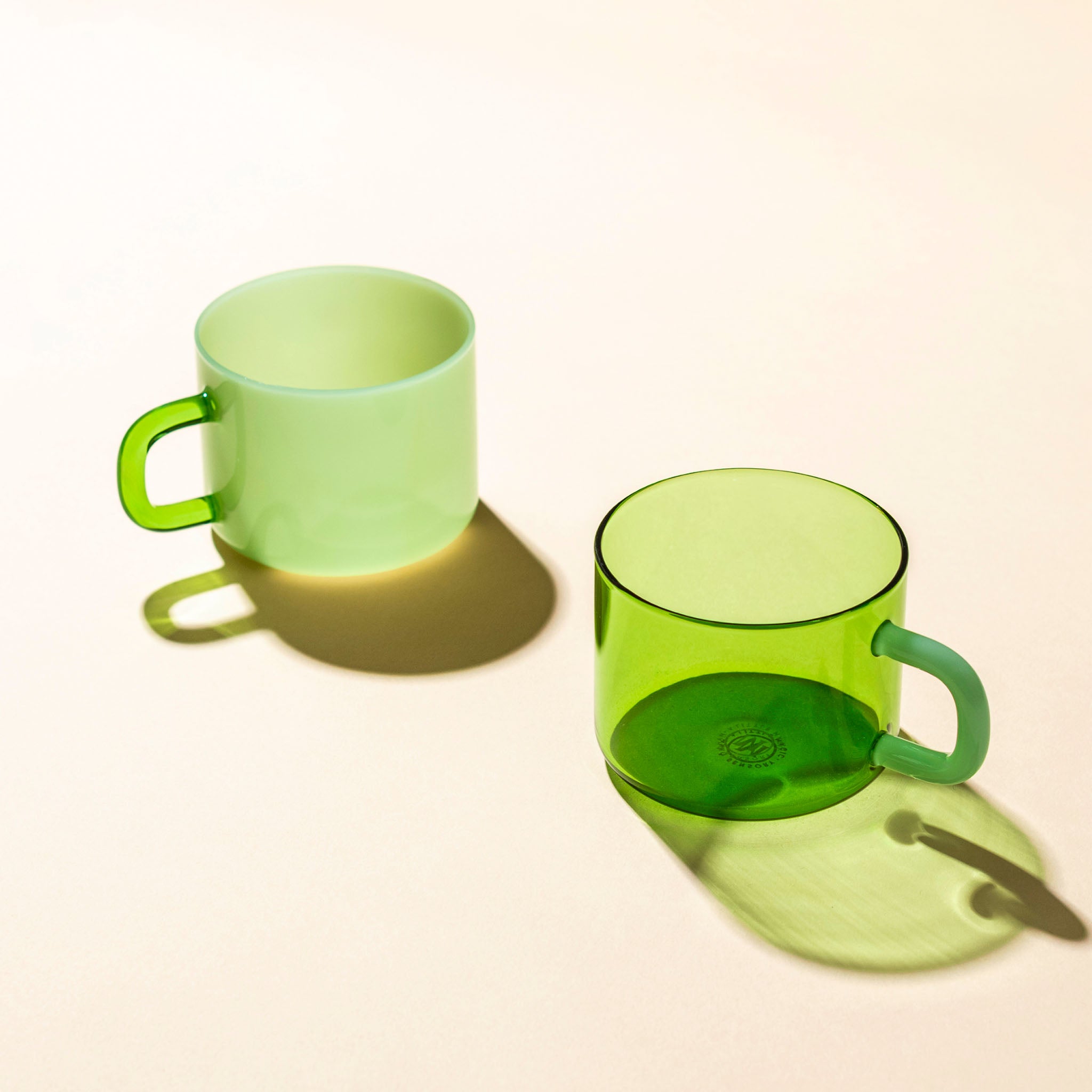 Two green mugs, one ceramic the other glass on a beige background