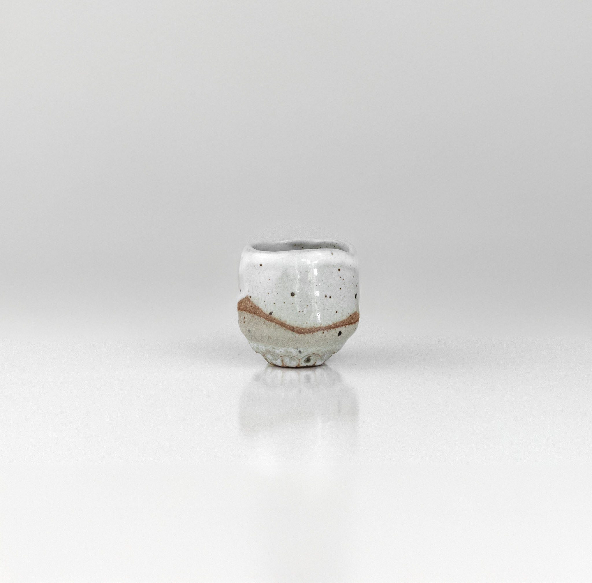Small handcrafted ceramic sake cup with white glaze and exposed clay band, made by The Lazy Potters.