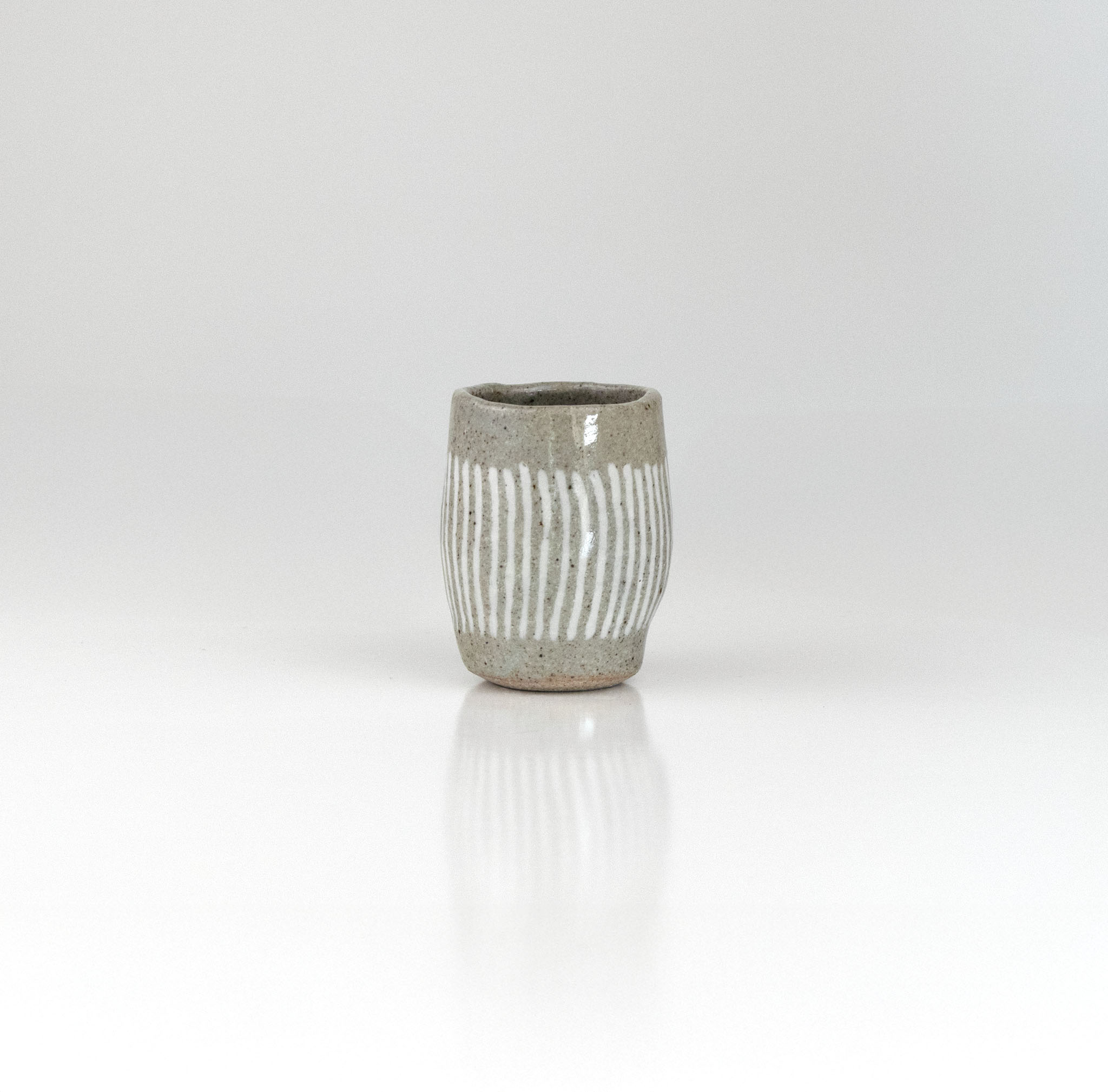 Hand-thrown ceramic sake cup with vertical white brush lines over grey glaze, by The Lazy Potters.