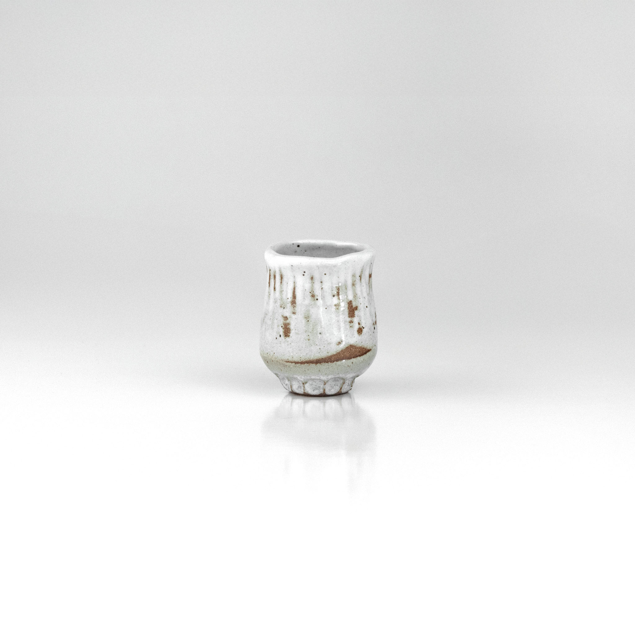 Handmade ceramic sake cup with white drip glaze and ribbed base in natural clay tones, by The Lazy Potters.