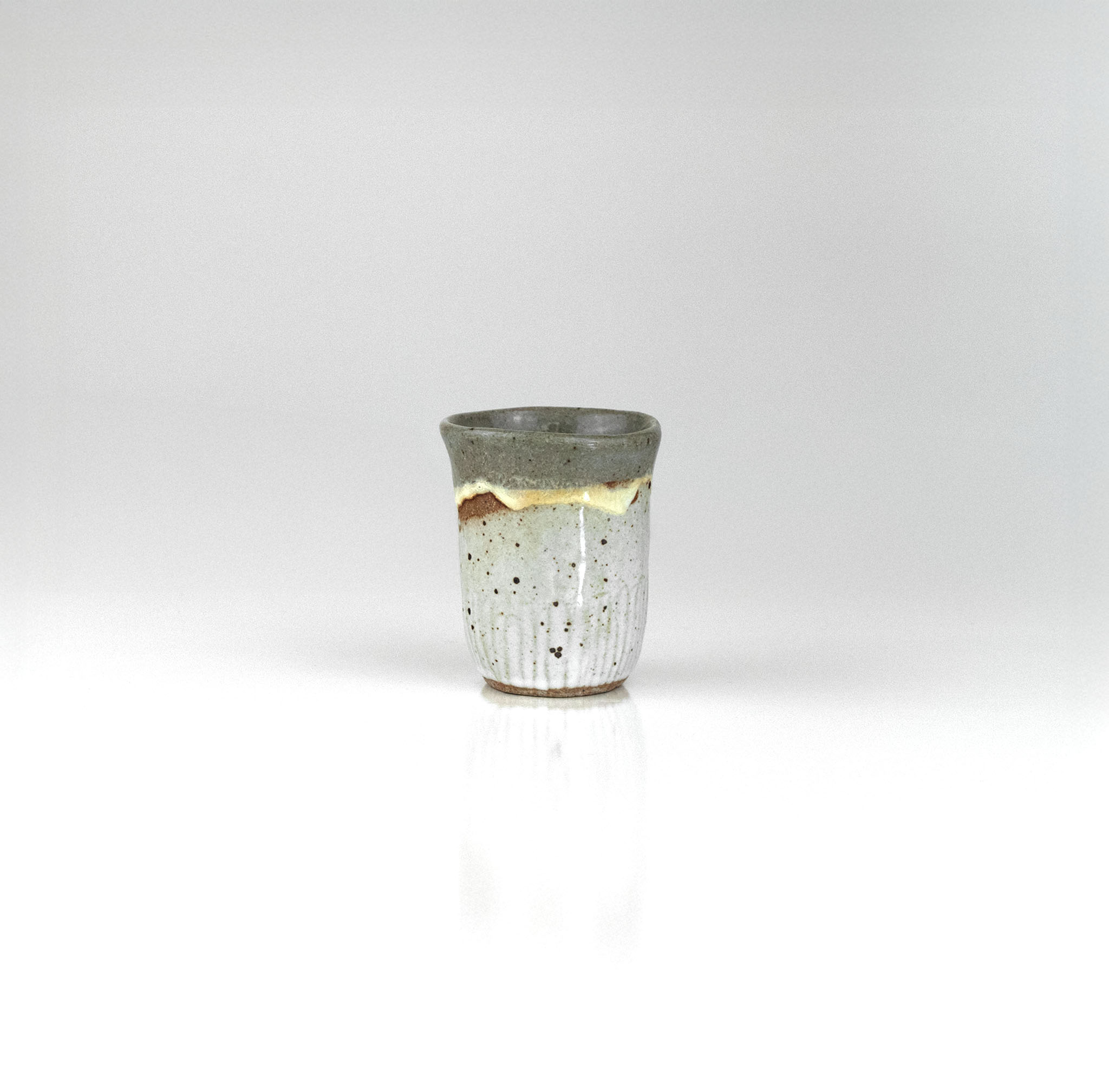 Handmade ceramic sake cup with layered grey and ochre glaze and speckled texture, by The Lazy Potters.