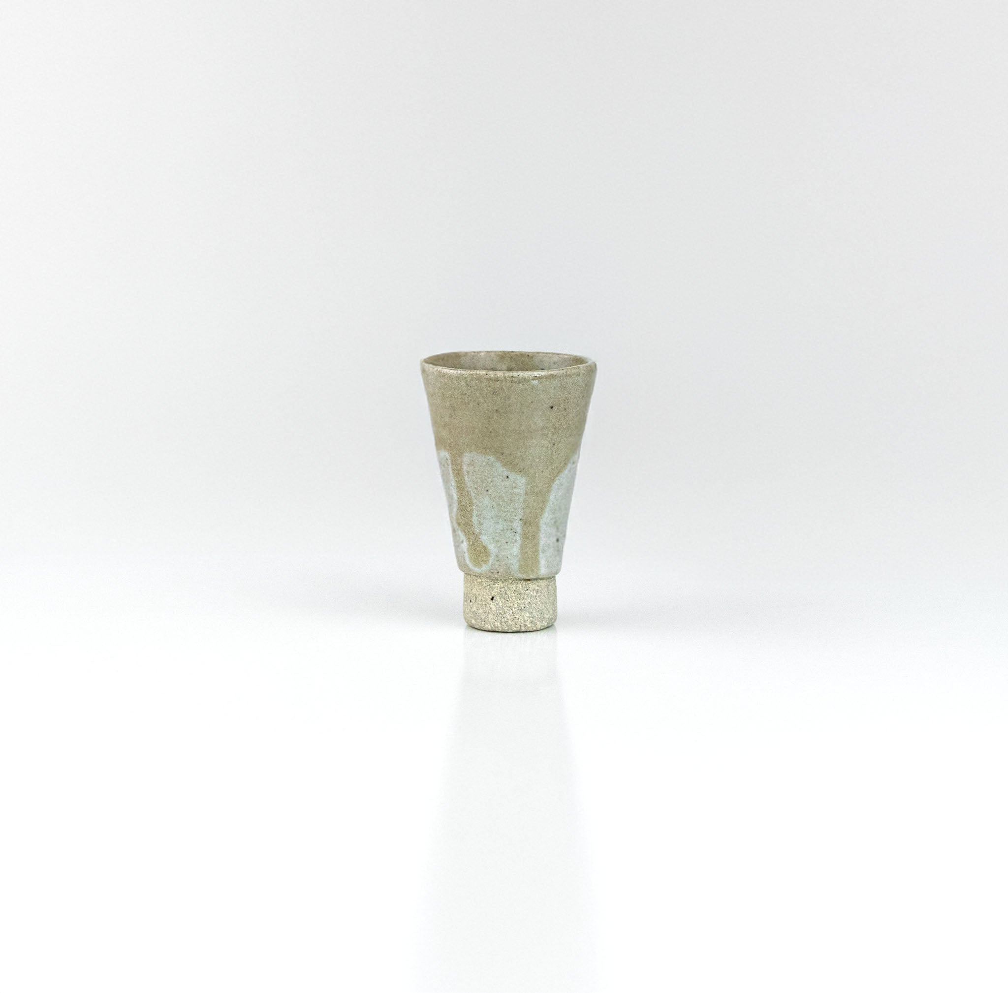 Tapered handmade ceramic sake cup with pale celadon glaze and raised clay foot, by The Lazy Potters.