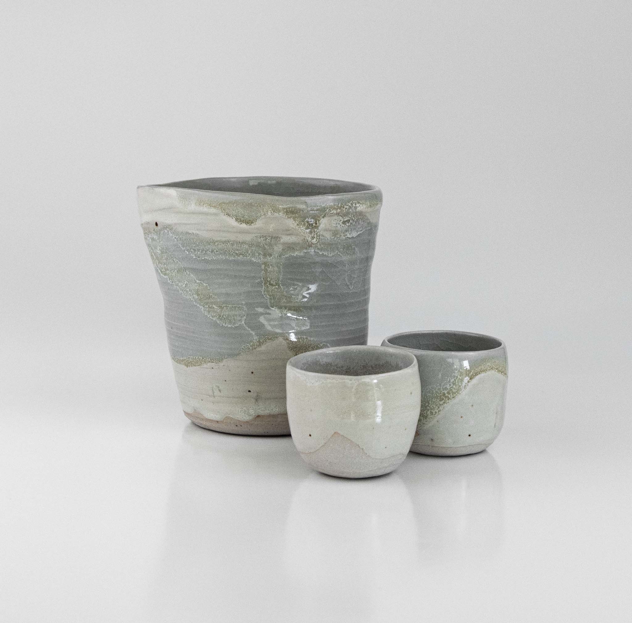 Handcrafted ceramic sake set with soft grey and celadon glaze, including a rounded pourer and two matching cups by The Lazy Potters.