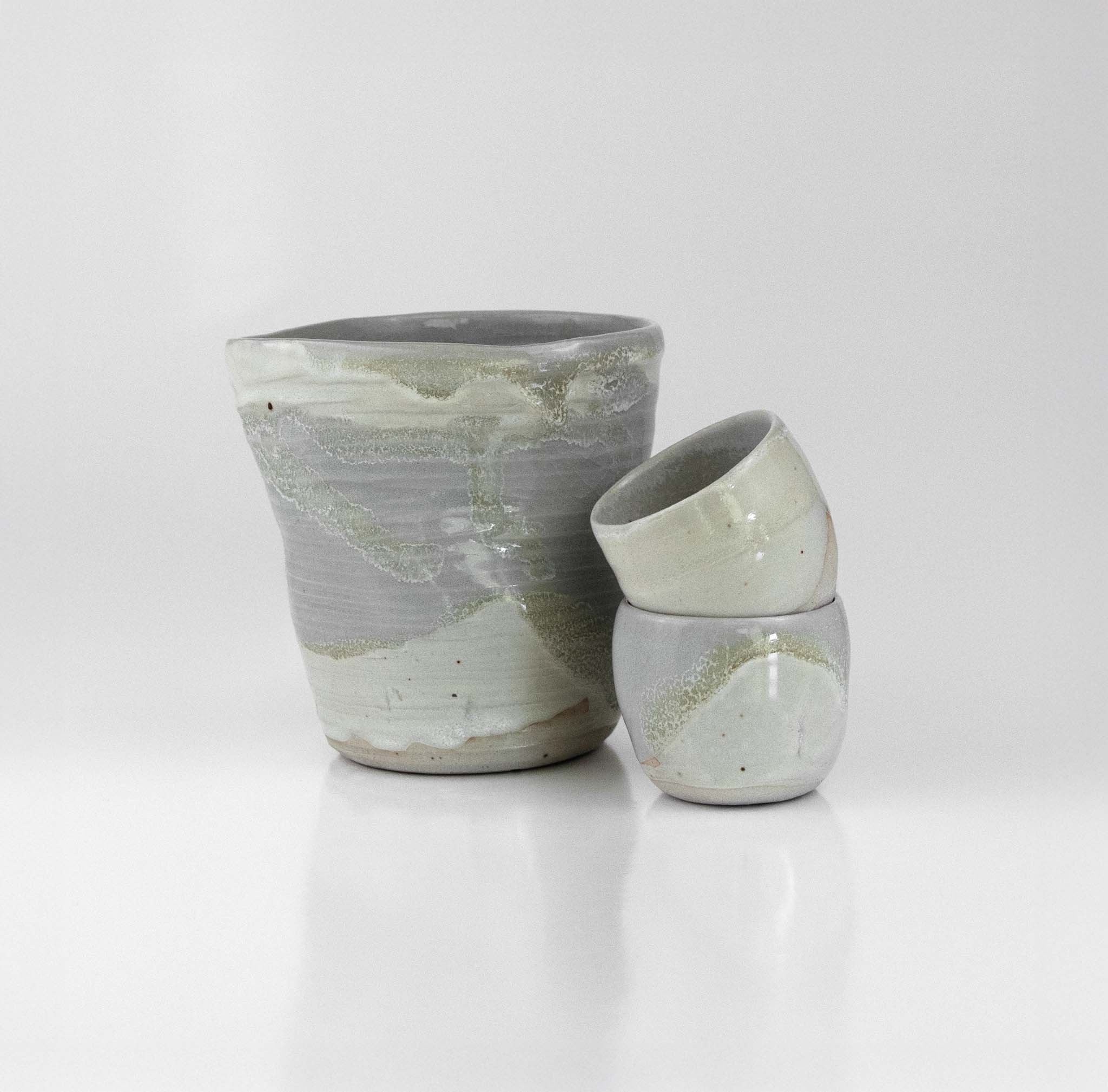 Handcrafted ceramic sake set with soft grey and celadon glaze, including a rounded pourer and two matching cups by The Lazy Potters.