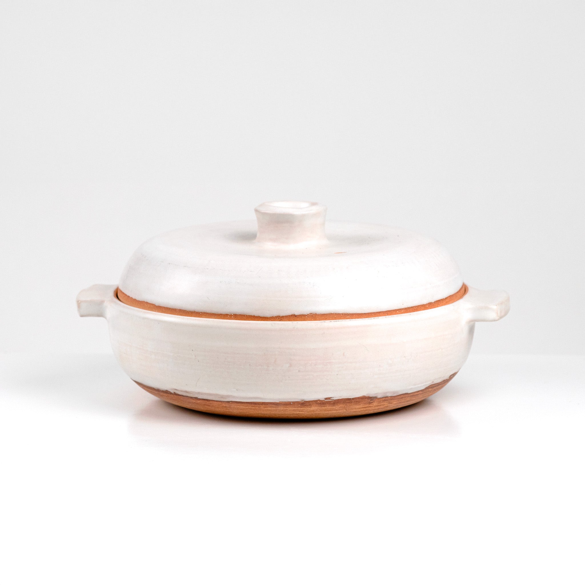 Limited edition off-white ceramic ttukbaegi  with terrapcotta colored rim on a white background