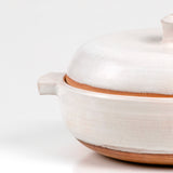 Close up of limited edition off-white ceramic ttukbaegi  with terrapcotta colored rim on a white background