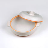 Limited edition off-white ceramic ttukbaegi with lid off showing inside of pot and the terrapcotta colored rim on a white background
