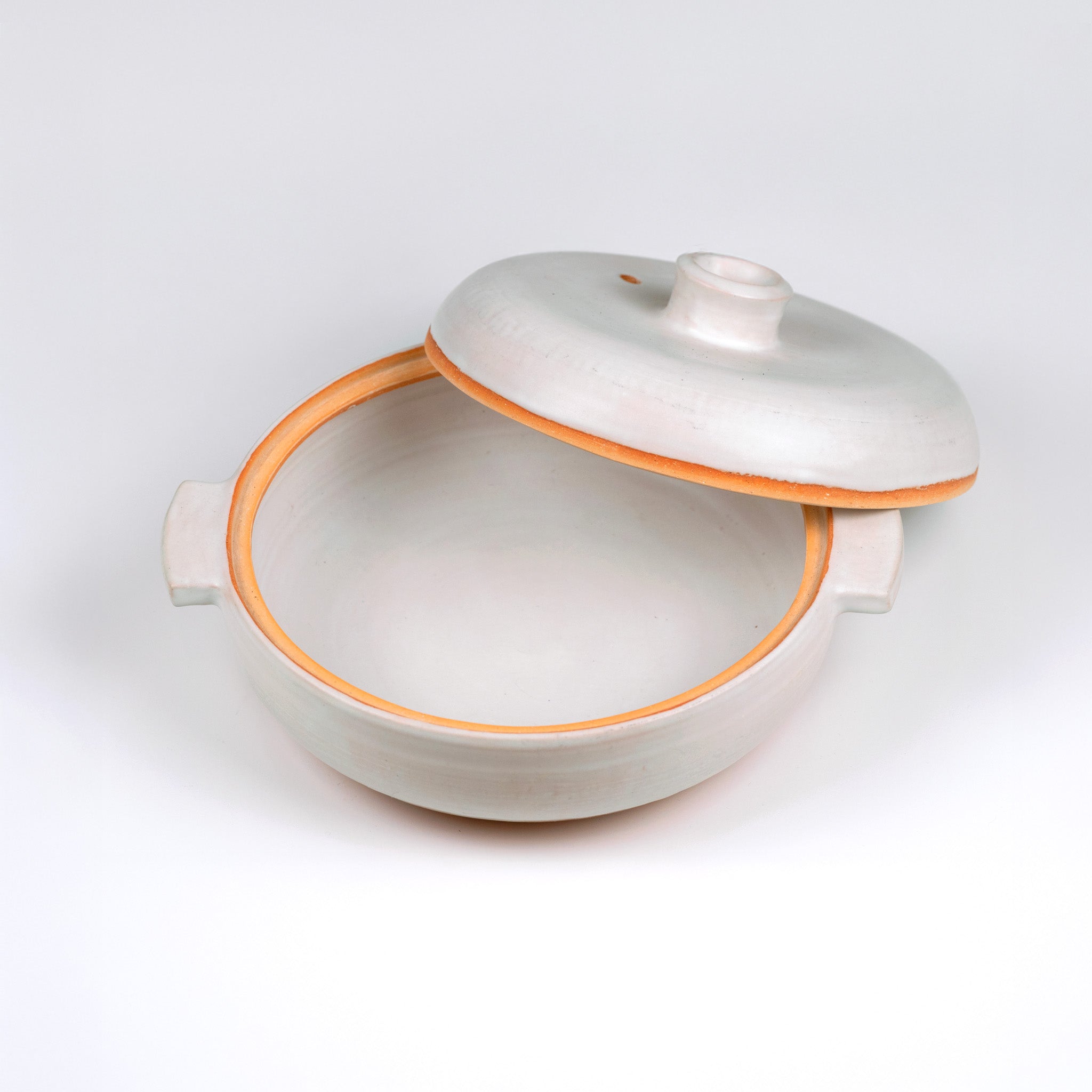 Limited edition off-white ceramic ttukbaegi with lid off showing inside of pot and the terrapcotta colored rim on a white background
