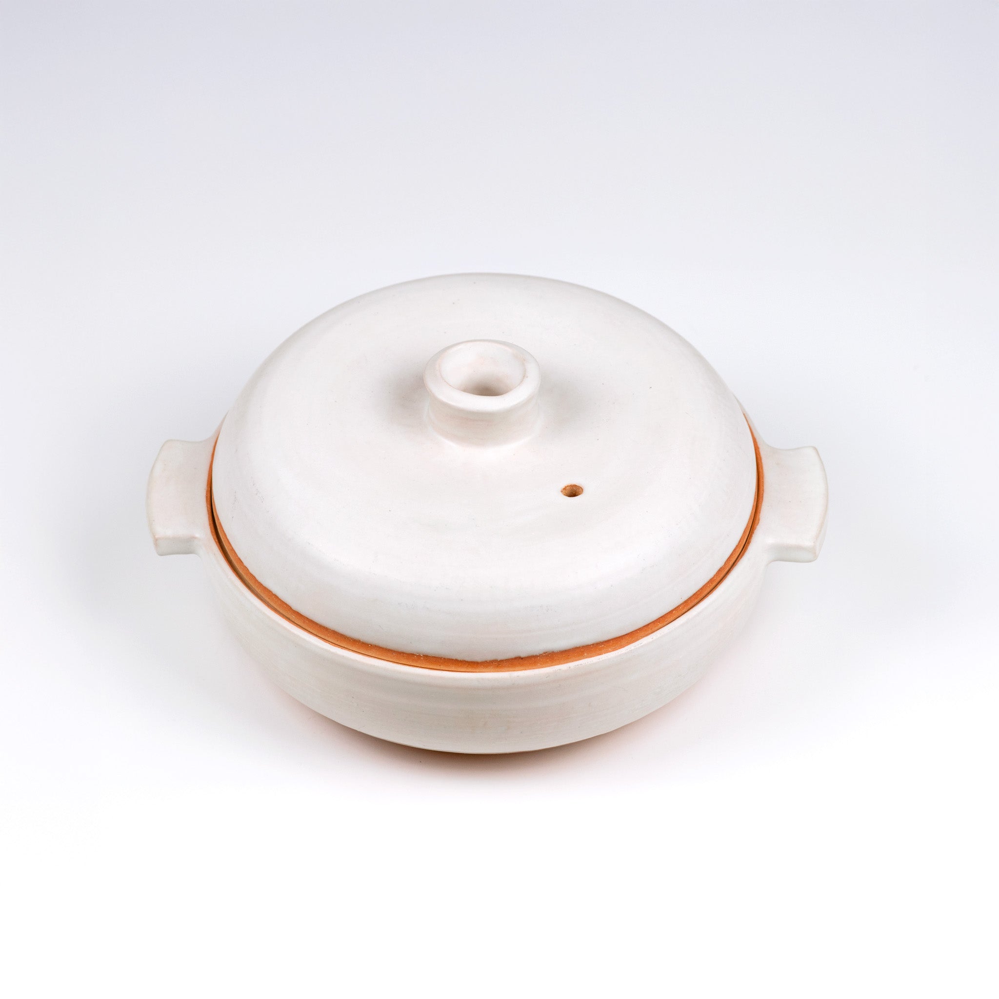 Limited edition off-white ceramic ttukbaegi  with terrapcotta colored rim on a white background