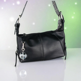 Black handbag with a round clear ball designed keychain on a gradient background