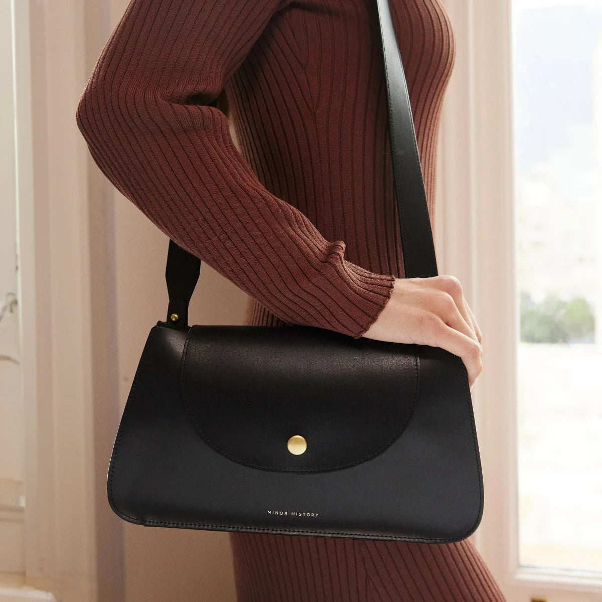 A side view of model carrying Minor History's The Horizon Crossbody bag in black