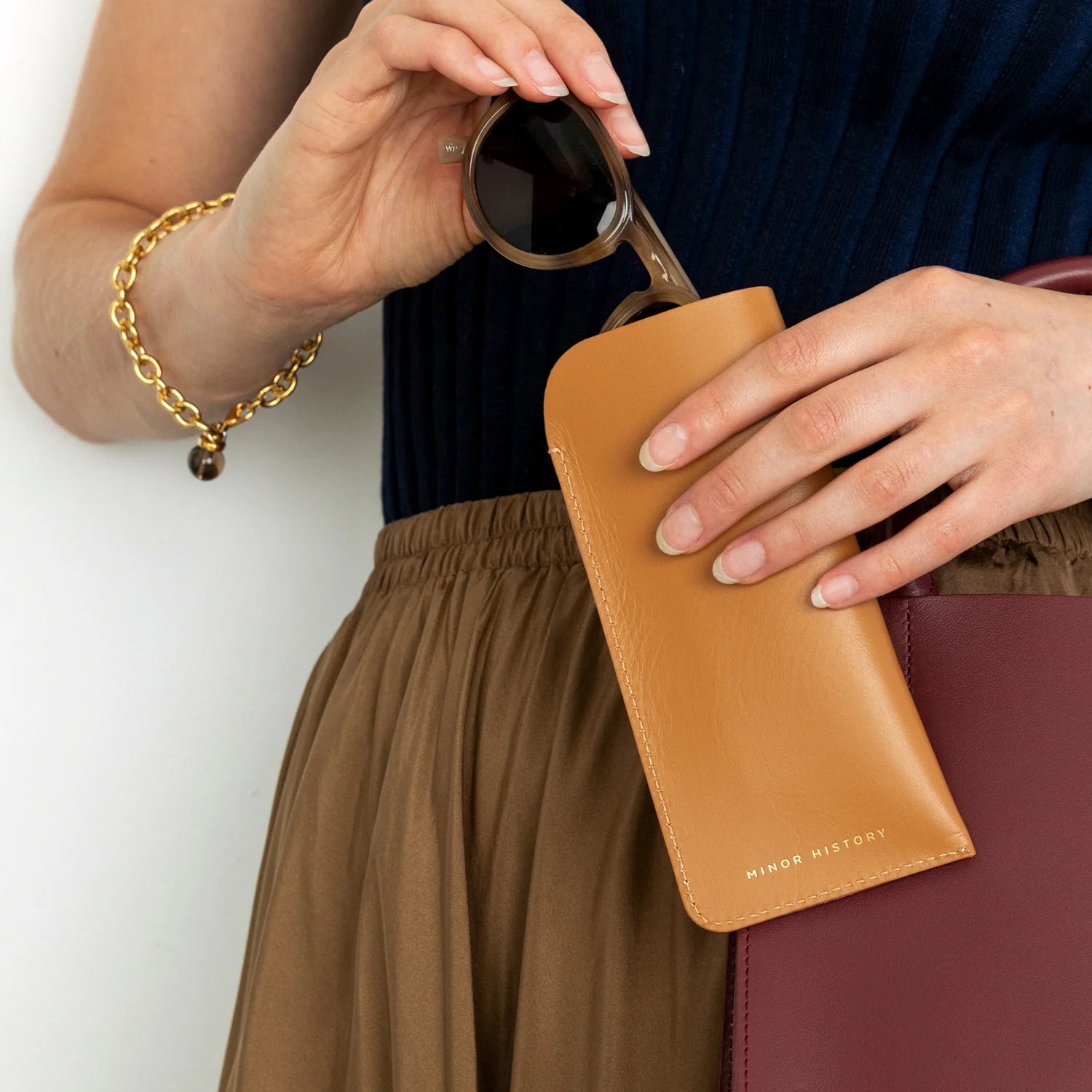 A hand model inserting a pair of glasses into The Looker Glass Case in color saddle