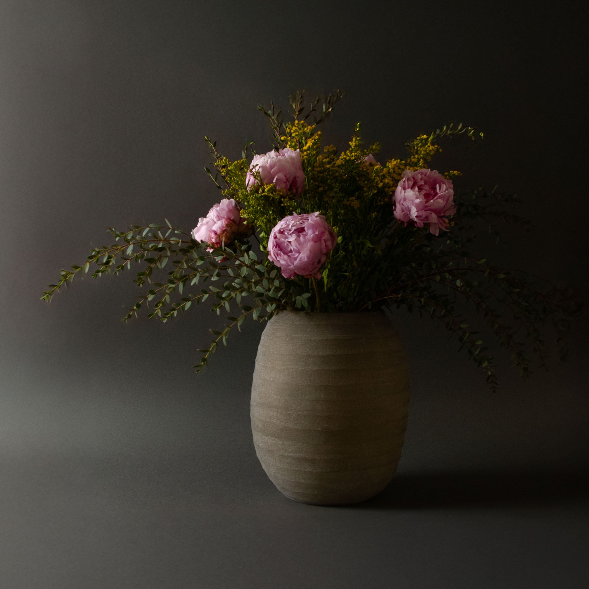 Image of sand colored vase showcasing a bouquet of pink and yellow flowers