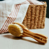 Wooden dog brush with bristles on a surface with a basket and towel in the background