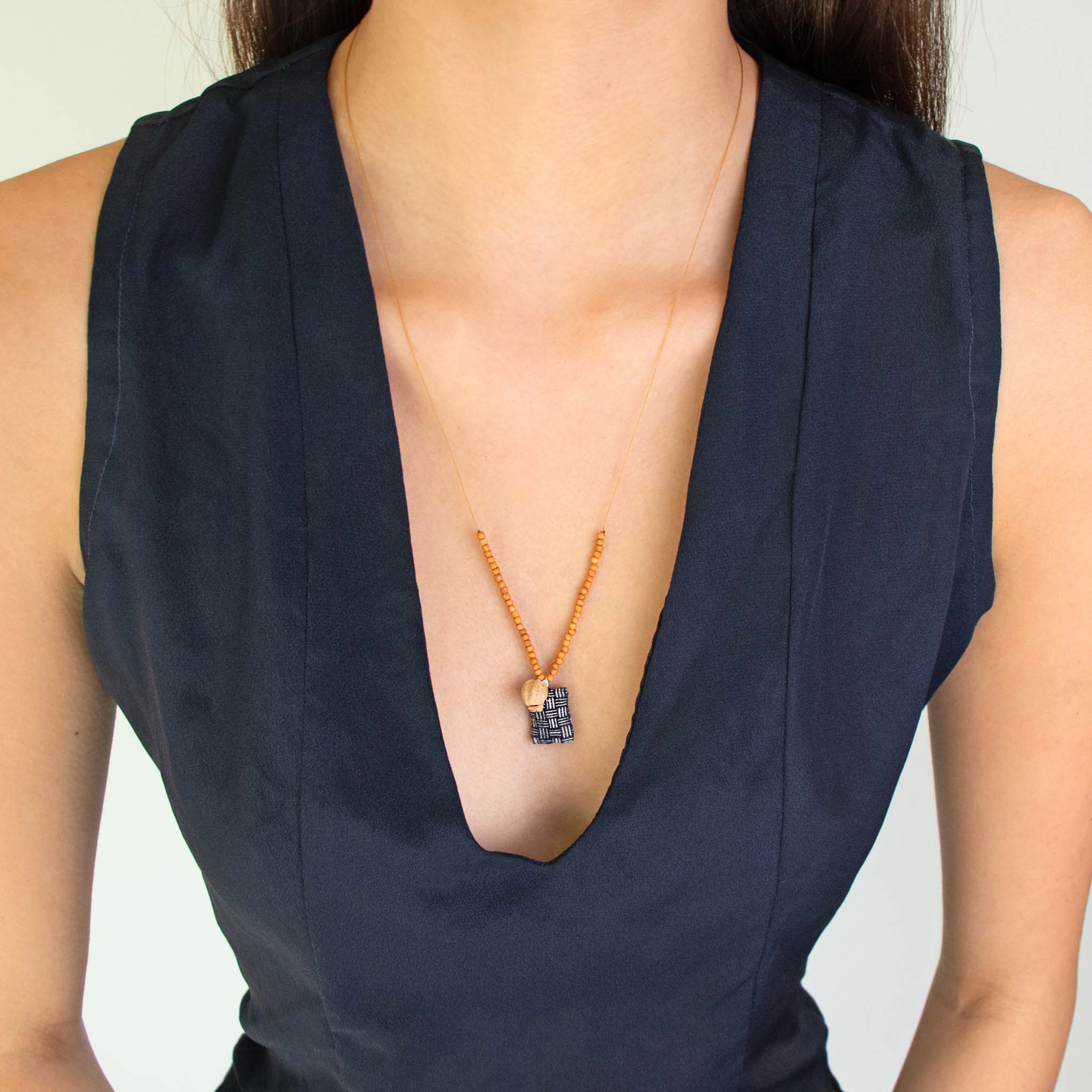 Person wearing a dark blue sleeveless top with See Real Flowers Trinket necklace in indigo.
