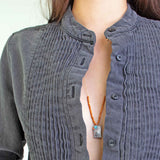 Person wearing a gray tuxedo shirt with See Real Flowers Trinket necklace in silver.