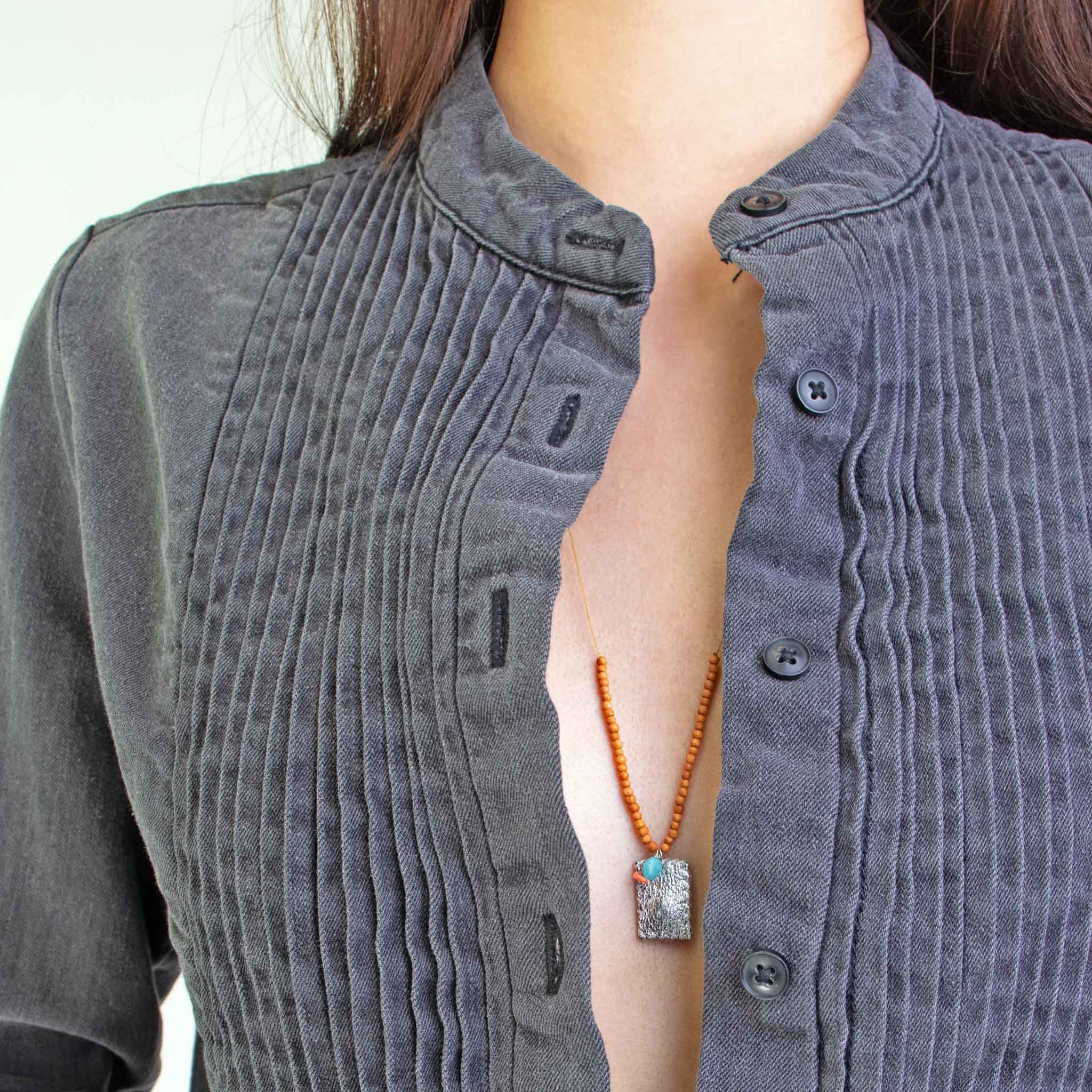 Person wearing a gray tuxedo shirt with See Real Flowers Trinket necklace in silver.