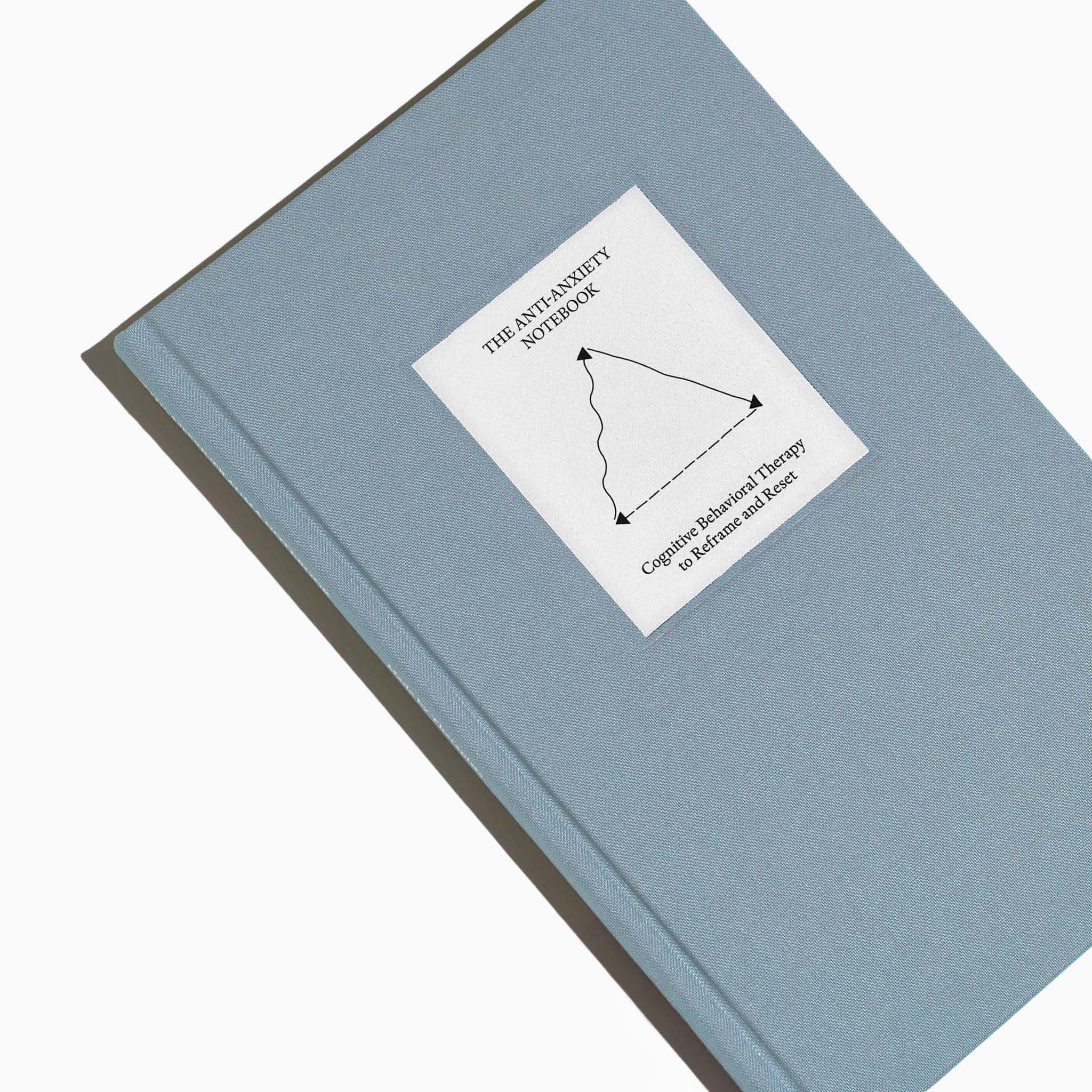 Top view of The Anti-Anxiety Notebook by Therapy Notebooks, featuring a linen hardcover with a minimalist stitched patch and embossed spine text.