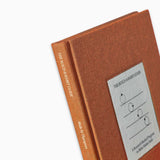 Close-up of The Build A Habit Guide by Therapy Notebooks, featuring a linen hardcover with a minimalist stitched patch and embossed spine text.