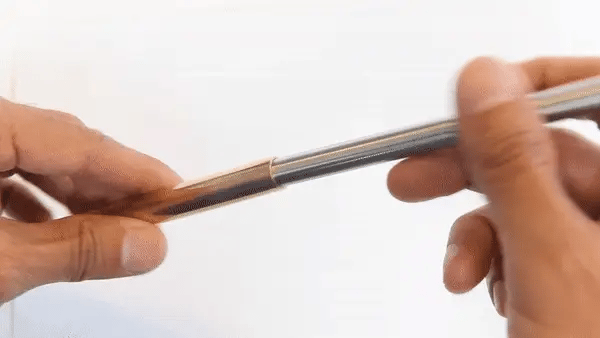 close-up of a person's hands holding a slim metallic pen that has a piston-like effect against a plain white background.