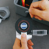 Person using a Penco label maker with a black label on a gray surface