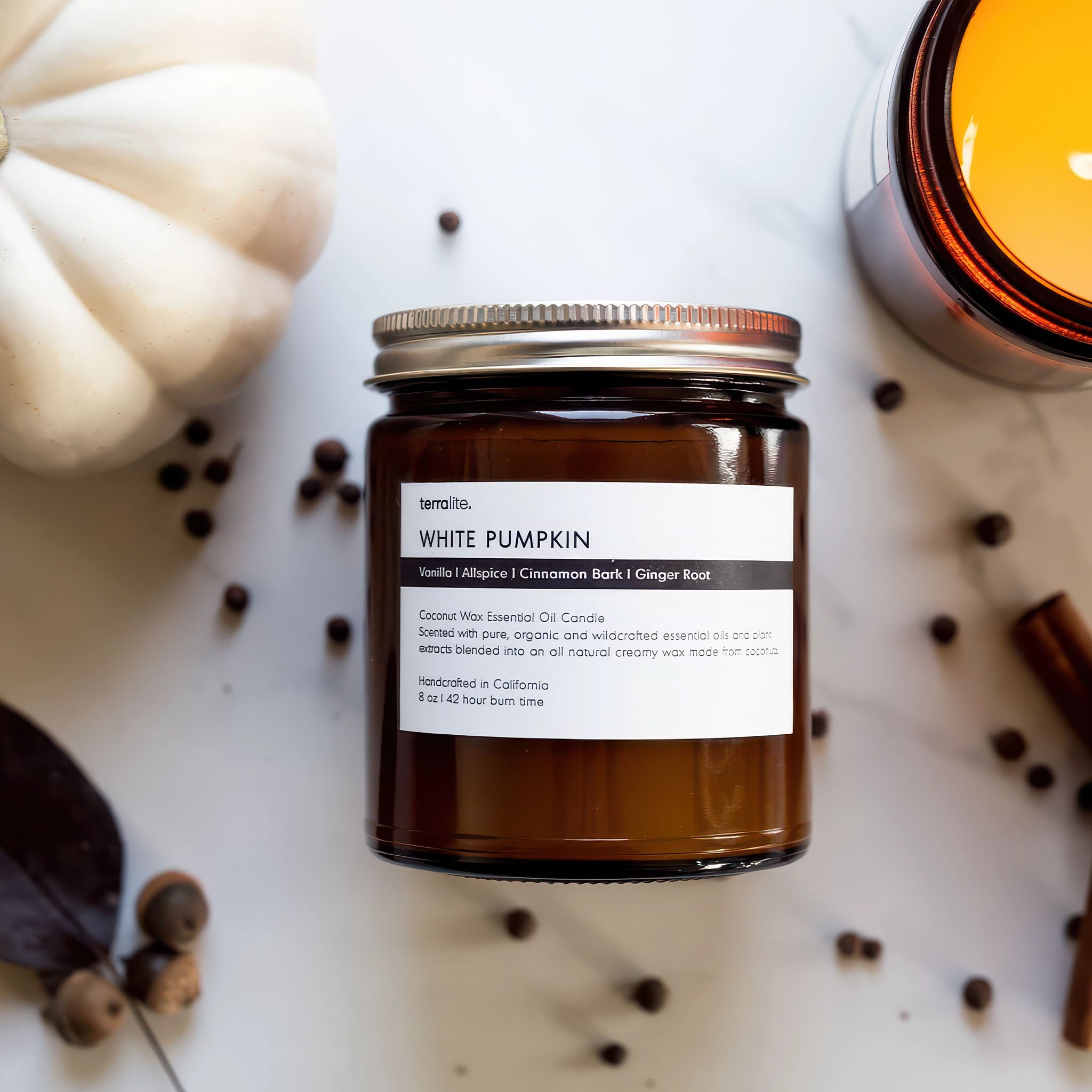 image of a jar of terralite scented candles white pumpkin scent with white pumpkin and a lit candle in the background