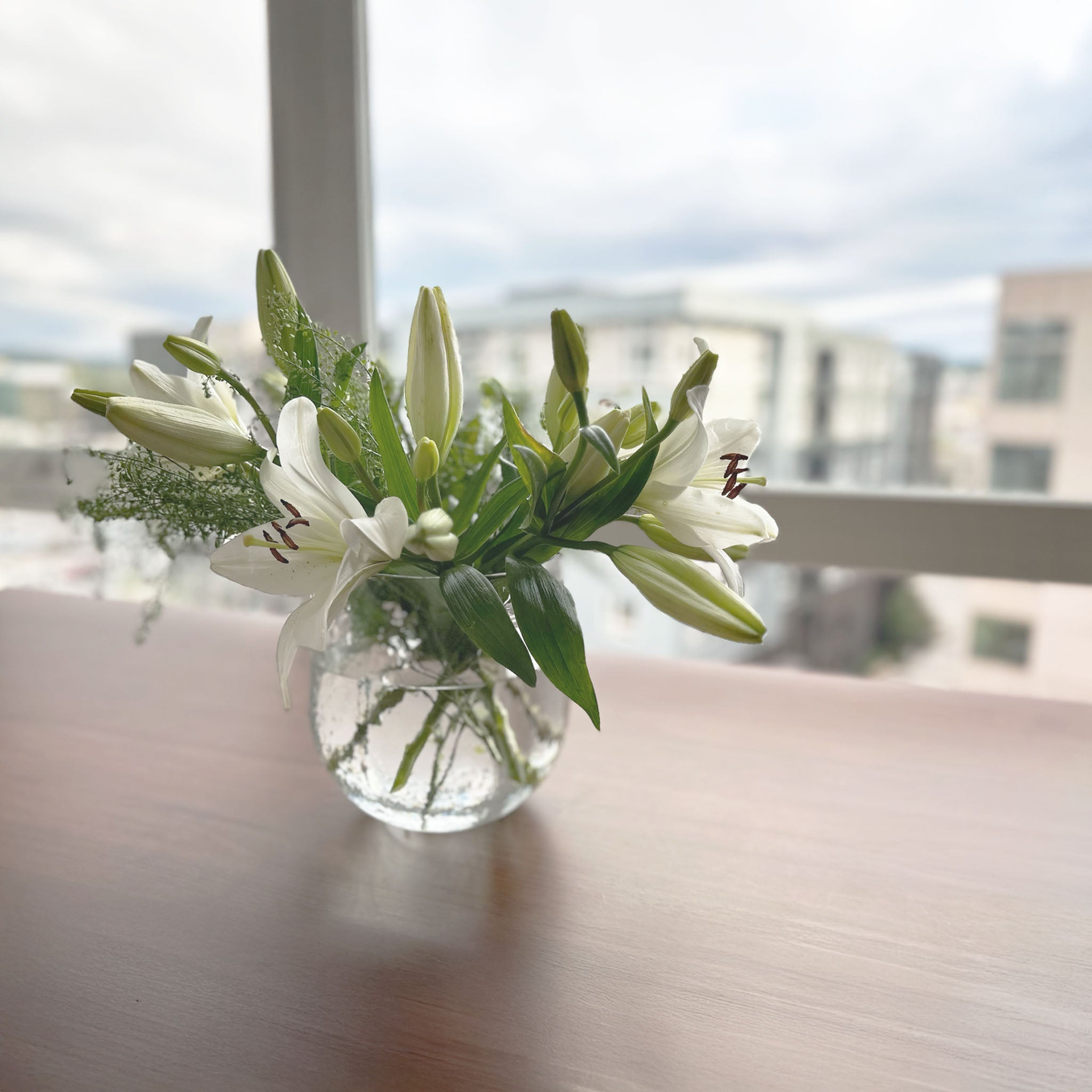 Hammered glass vessel repurposed as a vase with fresh white lilies and greenery on a windowsill.