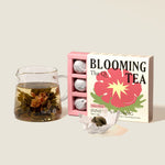 image of open box of the qi inner awakening blooming tea next to a tea pot