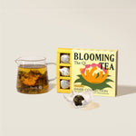 image of open box of the qi inner connection blooming tea next to a tea pot