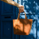 A hand model holds the Nimes Gorriti Saddle Handbag in front of a blue door